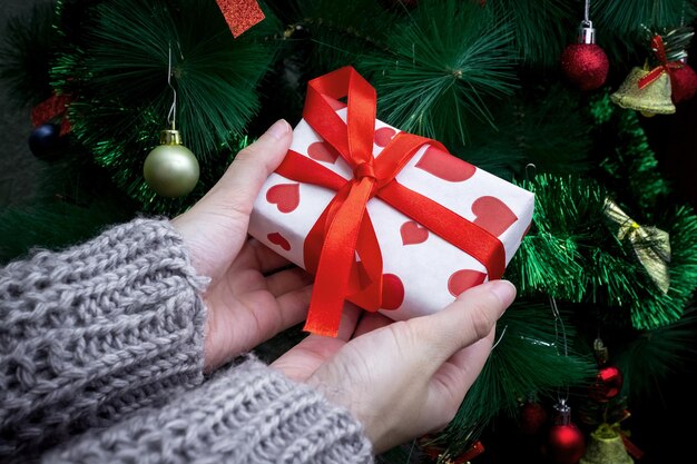 Caja de regalo en manos femeninas en el fondo del árbol de Navidad. Concepto de regalos de vacaciones.