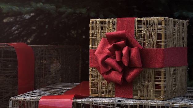 Foto caja de regalo de marco de alambre dorado envuelto con cinta roja debajo del árbol de navidad