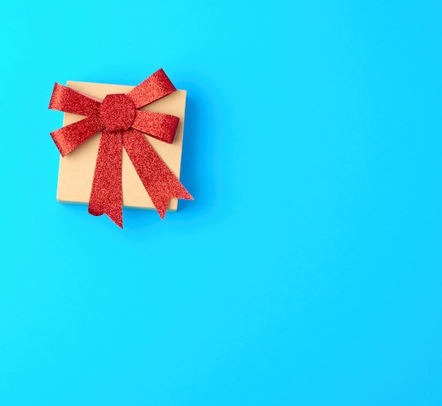 Caja de regalo marrón cerrada con un lazo rojo brillante sobre un azul