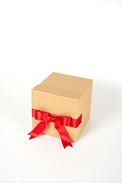 Caja de regalo marrón con una cinta roja sobre un fondo blanco.