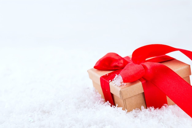 Caja de regalo marrón decorativa con un gran lazo rojo de pie en la nieve fresca