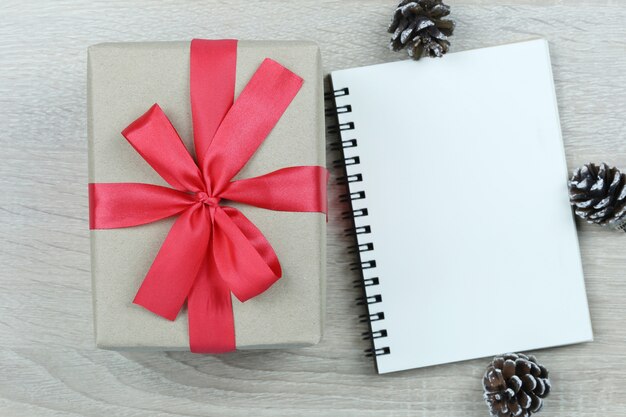 Caja de regalo marrón con lazo rojo en el piso de madera y libro en blanco en Navidad y año nuevo conce