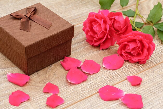 Caja de regalo marrón, pétalos de rosa y hermosas rosas en el fondo de madera. Concepto de regalar en vacaciones. Vista superior.