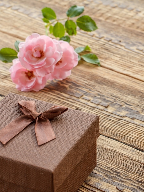 Caja de regalo marrón sobre viejas tablas de madera decoradas con rosas rosadas. Vista superior.