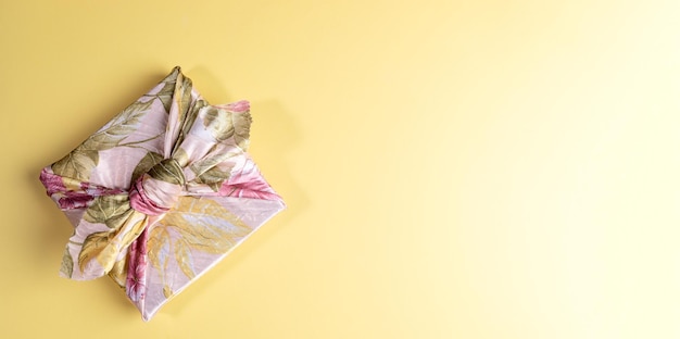 Una caja de regalo de moda envuelta en tela floral en la técnica japonesa furoshiki sobre fondo amarillo