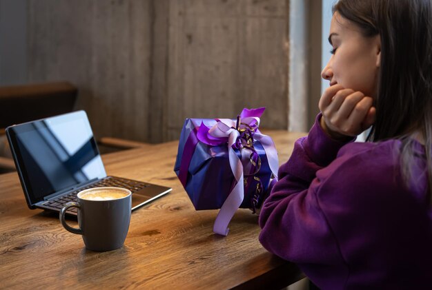 Caja de regalo morada en manos de una mujer con un suéter morado