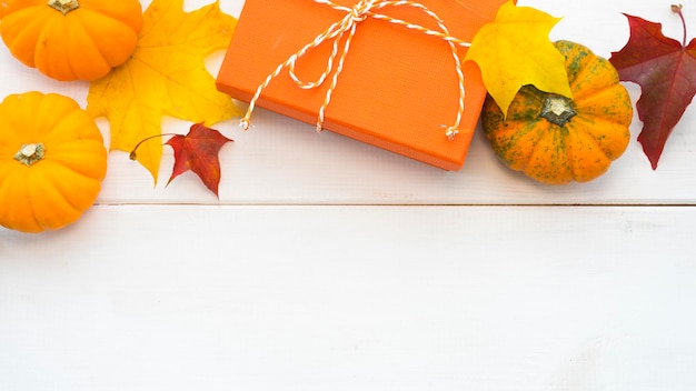 Caja de regalo naranja, calabazas y hojas de otoño sobre un fondo claro