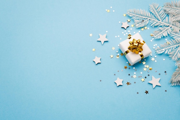 Caja de regalo de Navidad con adornos y destellos sobre fondo azul plano