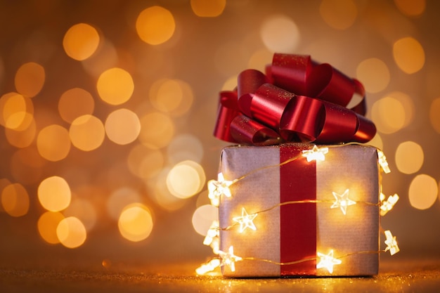 Caja de regalo de Navidad con cinta roja y luces sobre fondo dorado bokeh Tarjeta de felicitación navideña