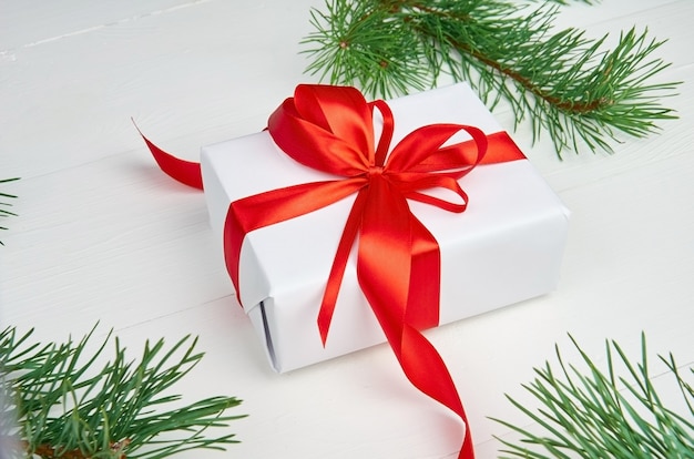 Caja de regalo de Navidad con cinta roja y ramas de pino sobre blanco