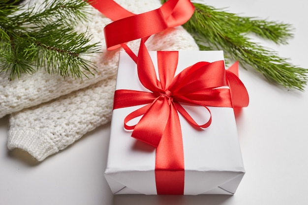 Caja de regalo de Navidad con cinta roja y suéter de punto con ramas de pino verde sobre blanco