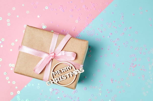 Caja de regalo de navidad con cinta rosa e inscripción feliz navidad con destellos navideños