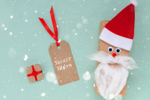 Caja de regalo de Navidad creativa en forma de gorro de Papá Noel y barba con etiqueta vacía y presente sobre fondo azul. Concepto secreto de Santa.