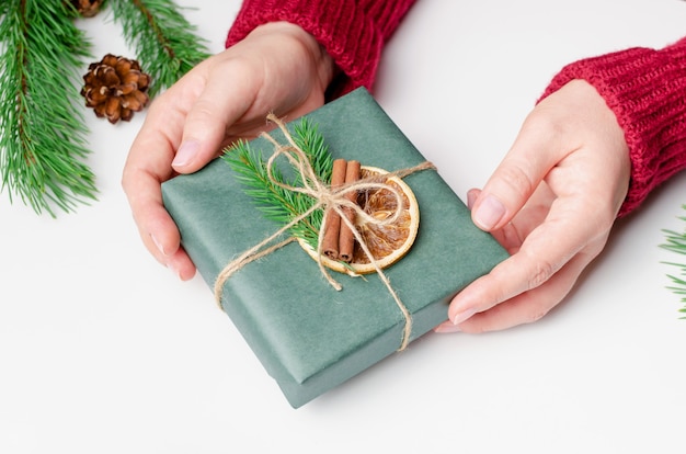 Caja de regalo de navidad decorada en manos femeninas sobre fondo blanco.