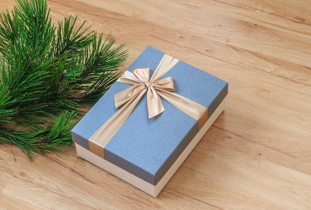 Caja de regalo de navidad con elegante cinta dorada cerca de ramas de pino verde en piso de madera