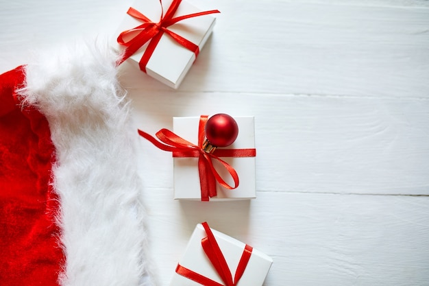 Caja de regalo de Navidad con gorro de Papá Noel, adornos rojos sobre fondo blanco de madera, Navidad, invierno, año nuevo concepto,