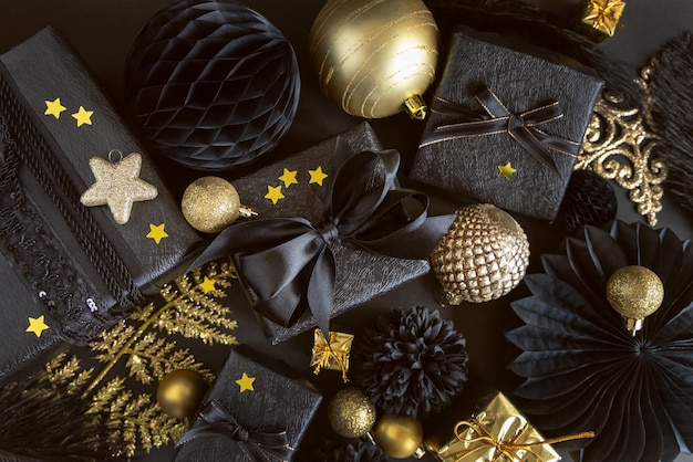 Caja de regalo de navidad con un lazo cerca de adornos y adornos negros y dorados vista superior