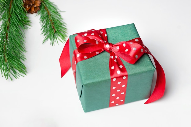Caja de regalo de Navidad con lazo rojo y rama de pino sobre blanco