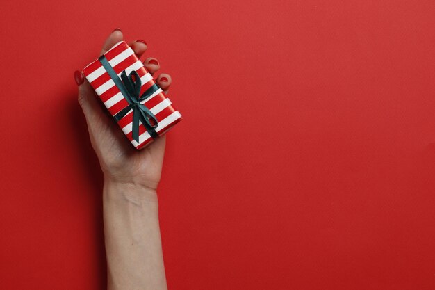 Caja de regalo de Navidad en una mano femenina sobre un fondo rojo. Lugar para el texto. Vista superior.