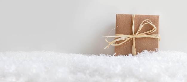 Caja de regalo de navidad en la nieve contra un fondo gris claro, concepto escandinavo de navidad blanco con c