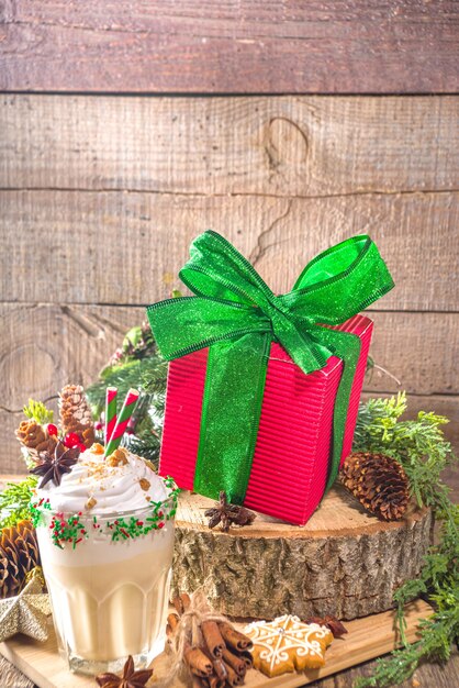 Caja de regalo de Navidad roja grande con cinta verde festiva brillante, sobre fondo tradicional de madera con decoración de Navidad y galletas de jengibre, espacio de copia