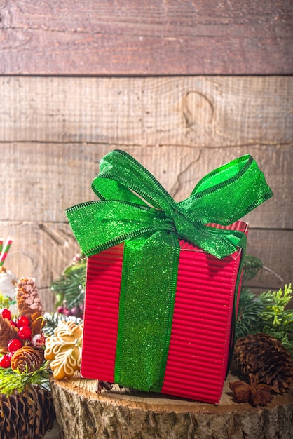 Caja de regalo de Navidad roja grande con cinta verde festiva brillante, sobre fondo tradicional de madera con decoración de Navidad y galletas de jengibre, espacio de copia