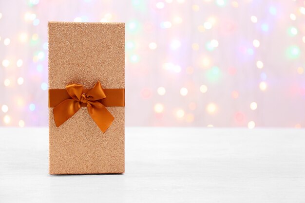 Caja con regalo de Navidad sobre superficie de madera contra luces desenfocadas