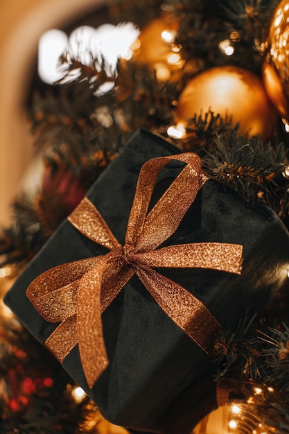 Caja de regalo de Navidad de terciopelo verde oscuro con una cinta dorada brillante colgando del árbol de Navidad