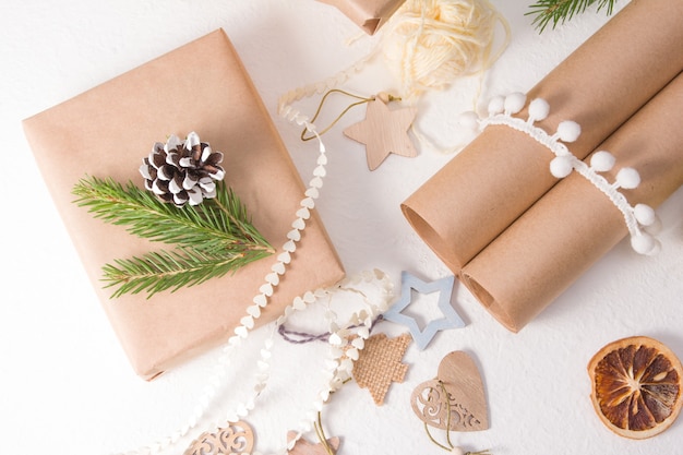 Caja de regalo navideña empaquetada en papel kraft y decorada con una rama de abeto fresco y una piña, materiales naturales para decorar regalos sobre un fondo blanco, concepto navideño ecológico