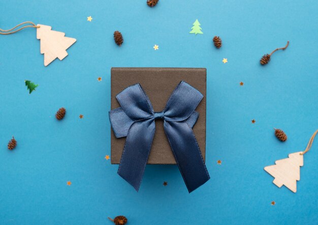 Caja de regalo negra con una cinta azul sobre un fondo azul claro con conos de estrellas y árboles de Navidad