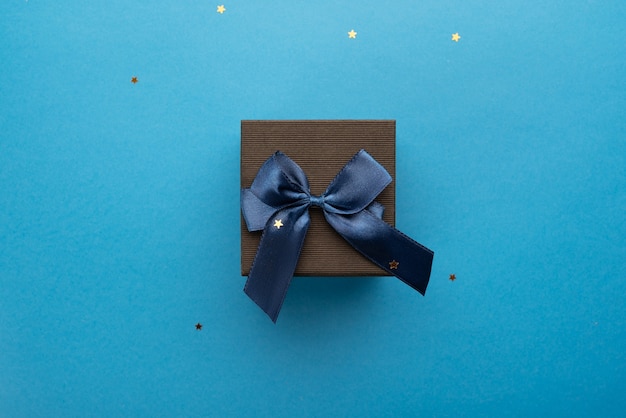 Caja de regalo negra con una cinta azul sobre un fondo azul claro con estrellas