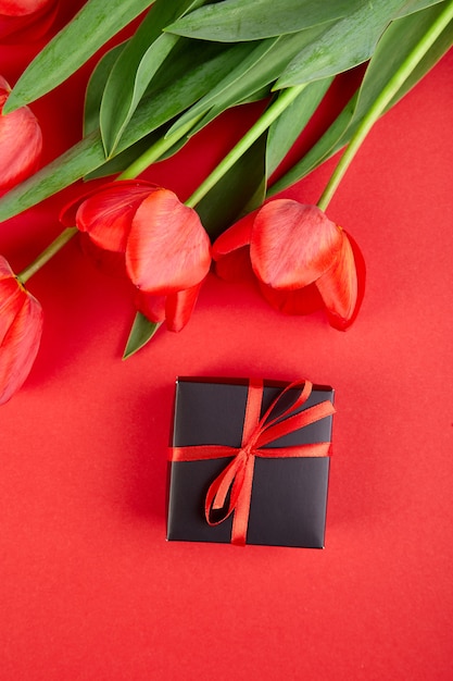 Caja de regalo negra con cinta roja cerca de tulipán rojo