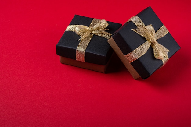 Caja de regalo negra con cintas doradas sobre papel rojo