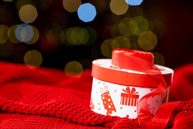 Caja de regalo para el nuevo año y una cinta roja sobre un plaid rojo tejido sobre un fondo oscuro con bokeh. Foto de alta calidad