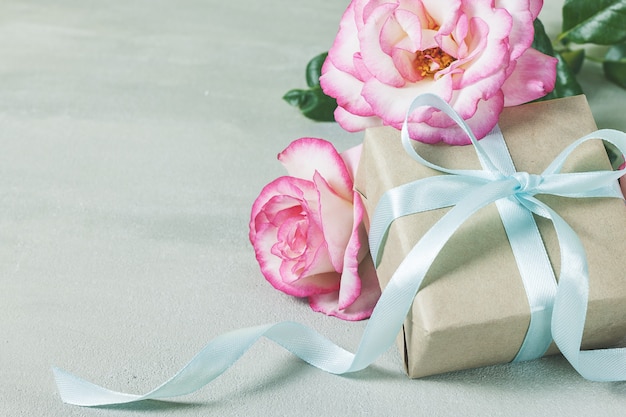 Caja de regalo o presente envuelta en papel artesanal y flor rosa rosa sobre mesa gris