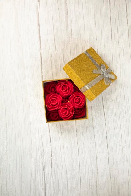 Caja de regalo o presente de oro con flores de rosas en el presente en la vista superior de la mesa de madera blanca ...