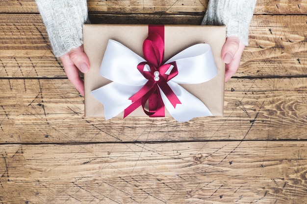 Caja de regalo o regalo con un gran lazo en las manos de una mujer con un suéter. Composición plana para Navidad, cumpleaños, día de la madre o boda.