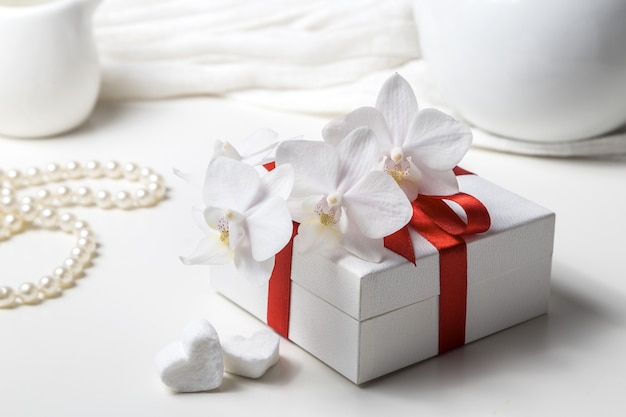 Caja con regalo y orquídea blanca sobre fondo blanco.