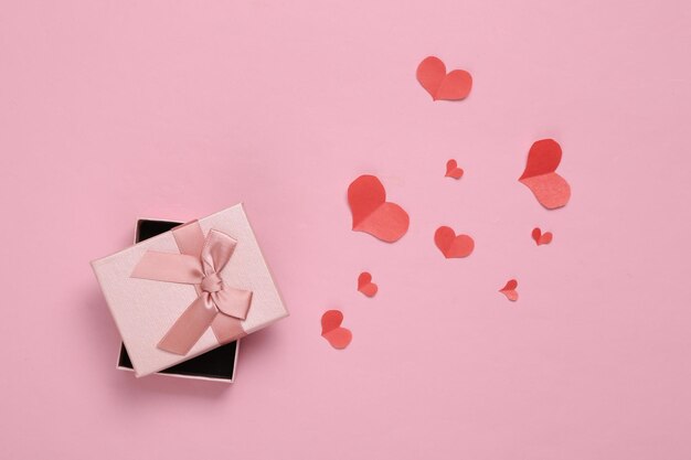 Caja de regalo con papel cortado Corazones rojos sobre fondo rosa Concepto de día de San Valentín Vista superior