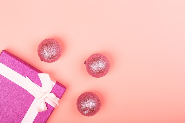 Caja de regalo con purpurina rosa con cinta y juguetes navideños sobre un fondo rosa. Fondo navideño minimalista con lugar vacío para texto.