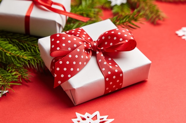 Caja de regalo con rama de árbol de Navidad y copos de nieve blancos sobre fondo rojo.