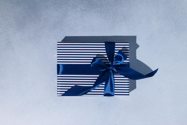 Caja de regalo de rayas azules y blancas con lazos azules sobre fondo gris Espacio de copia Mockup Flat lay