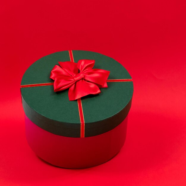 Foto caja de regalo redonda con un lazo rojo en una tapa verde sobre un fondo rojo vista lateral