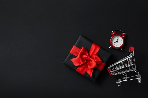 Caja de regalo, reloj despertador y carro de la tienda en negro