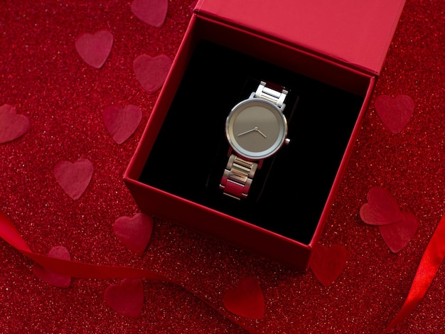 Foto caja de regalo con reloj de plata sobre fondo de papel de corazón rojo