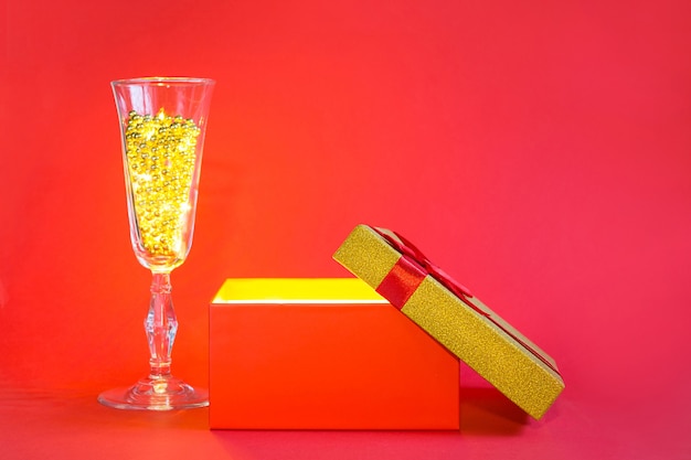 Caja de regalo roja abierta con brillo dorado y brillo en el interior y copa de champán con cuentas de burbujas, pancarta, copyspace
