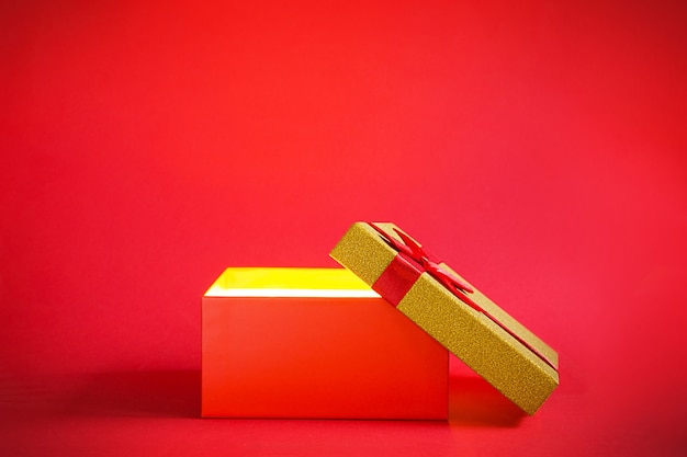 Foto caja de regalo roja abierta con un brillo dorado sobre un fondo rojo.