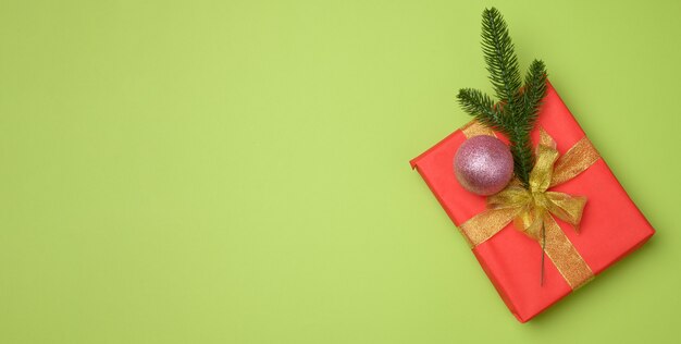 Caja de regalo roja atada con cinta roja sobre un fondo verde, vista superior. Telón de fondo festivo, espacio de copia