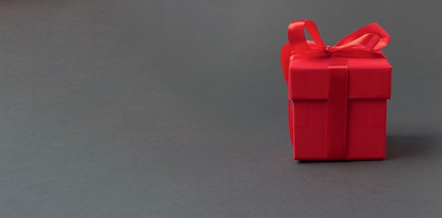 Caja de regalo roja atada con cintas con arcos sobre fondo gris