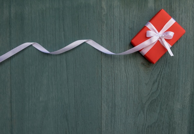 Caja de regalo roja con cinta blanca sobre fondo de madera verde